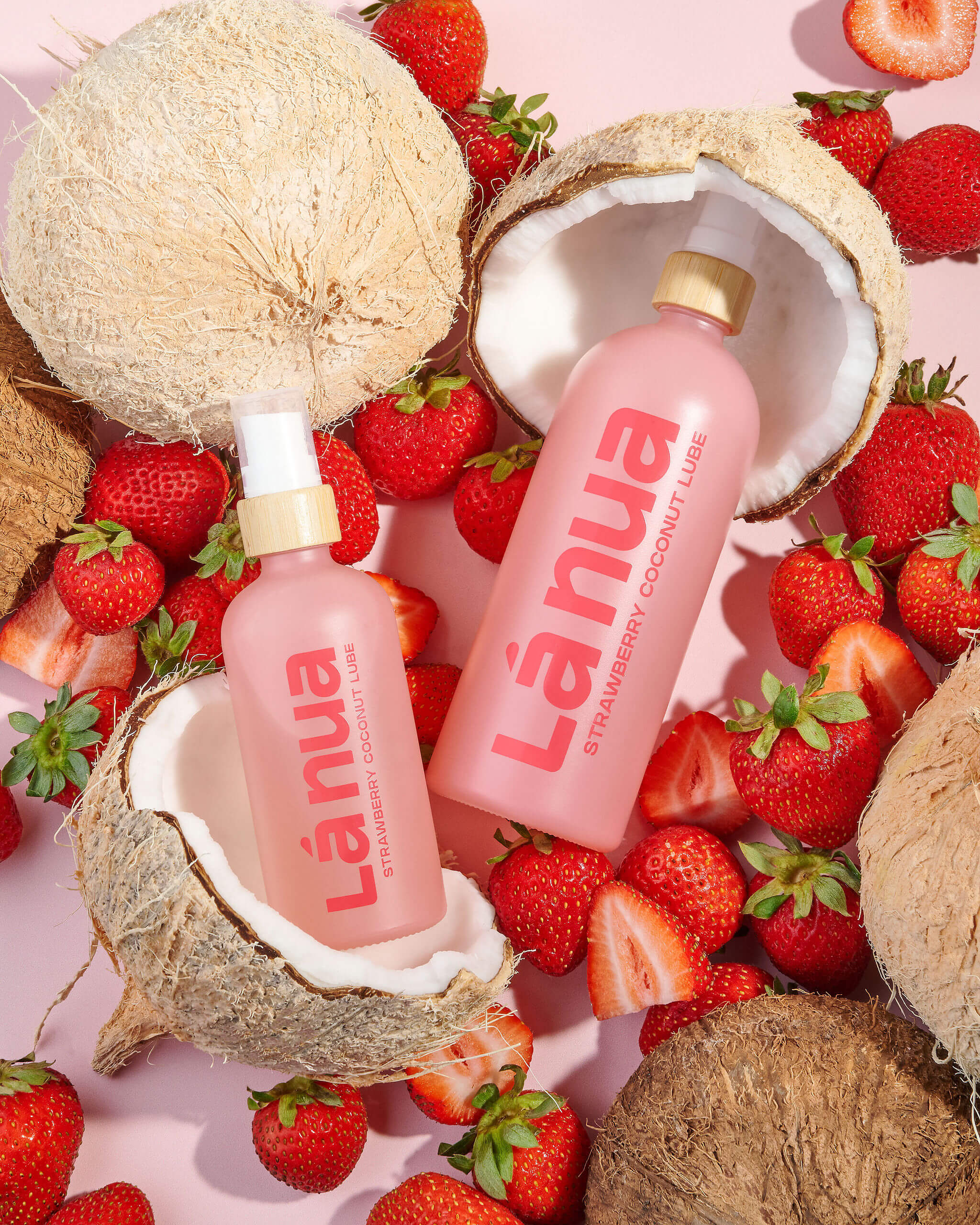 Two pink bottles of Lanua coconut water surrounded by coconuts and strawberries on a pink background