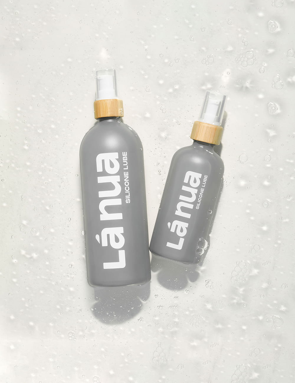 Two gray bottles of La nua silicone lube on a light gray background