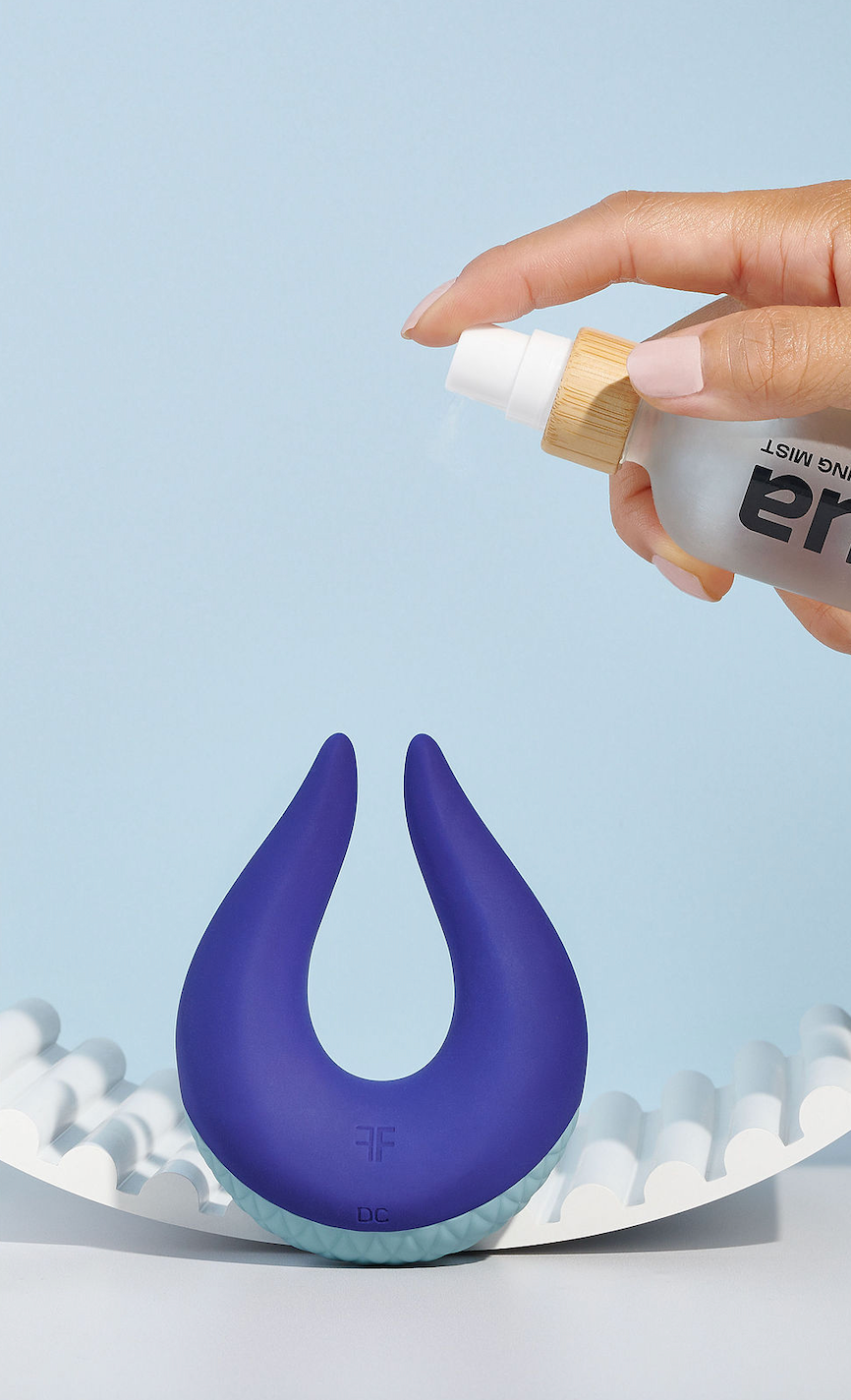 Purple silicone vibrator with a hand holding a toy cleaner bottle labeled la nua on a light blue background