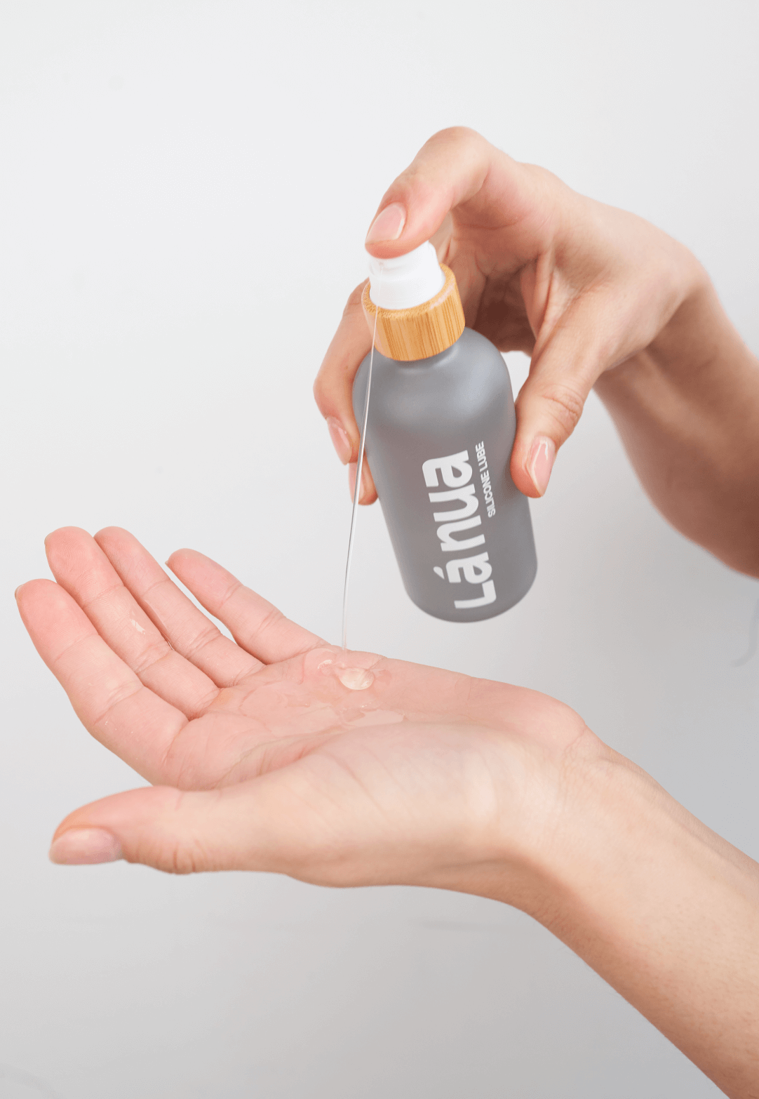 Person holding a small bottle of silicone lube labeled La nua above their palm with a light gray background